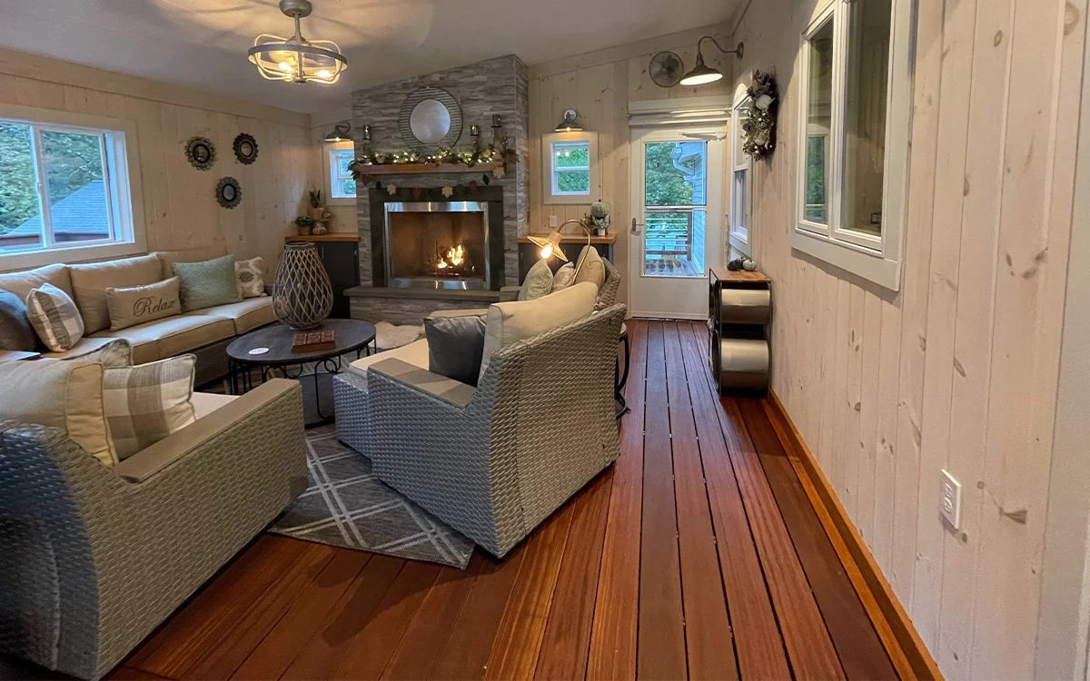 Enclosed porch with reddish balau floor and a lit fireplace