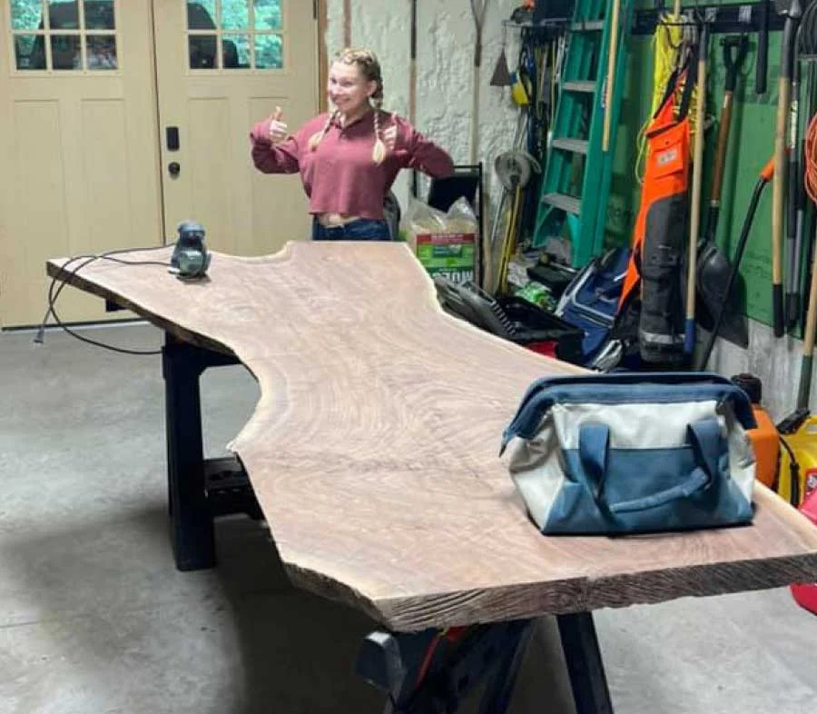 Woman giving thumbs up behind a slab tabletop on sawhorses in a garage