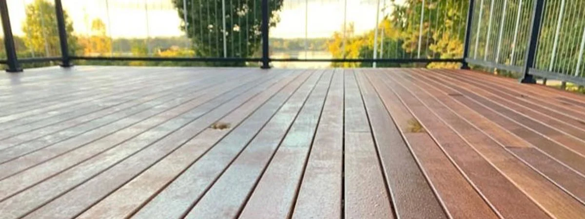 Low view along a deck toward a glass railing and sunset lake