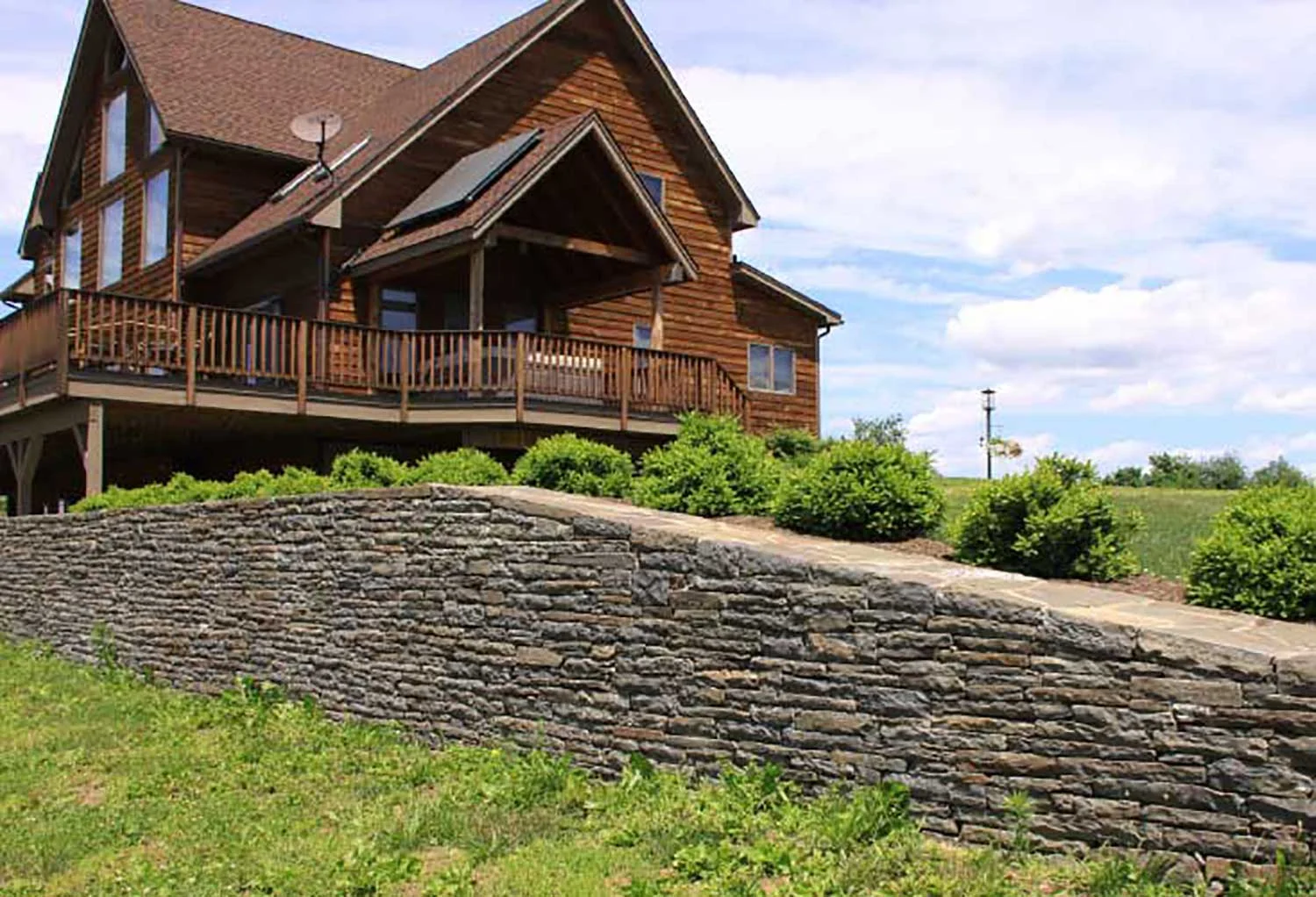 Wood-sided home with a deck, above a dry-laid bluestone retaining wall