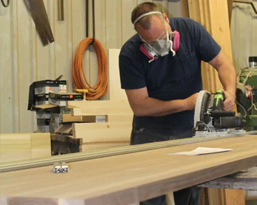 Millworker in a respirator sanding a long board in the shop