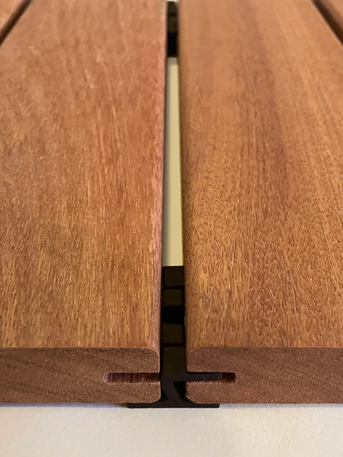 Black hidden clip seated in the grooves between two hardwood deck boards